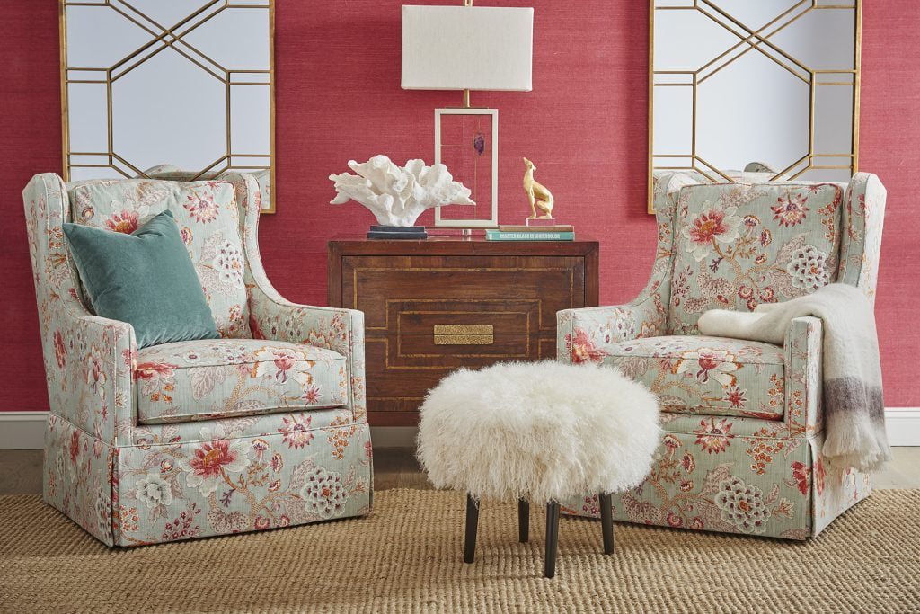 bountiful pink and green floral chairs in room with bright pink wallpaper and shaggy foot stool