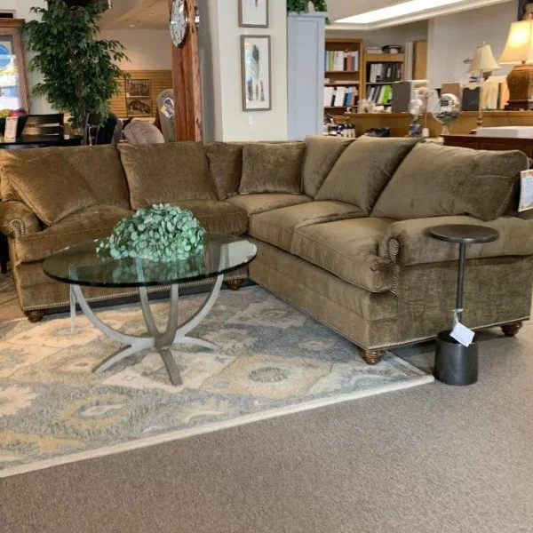 Brown fabric sectional with a round glass coffee table in front with a plant on top. Inside Egger's showroom.