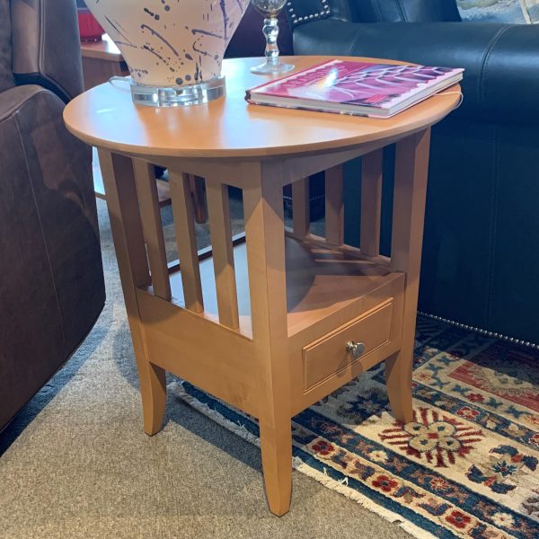 Wooden end table with round top and square bottom with drawer. Small metal knob to open drawer along with decor on top of table.