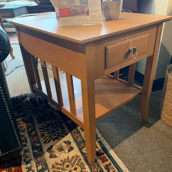 Wooden end table with square top and bottom with drawer. Small metal knob to open drawer along with decor on top of table.