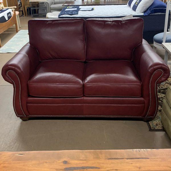 Red leather seat that fits two people. Metal pins in silver outline the arm chairs and bottom edge of couch when looking at it from a front view.