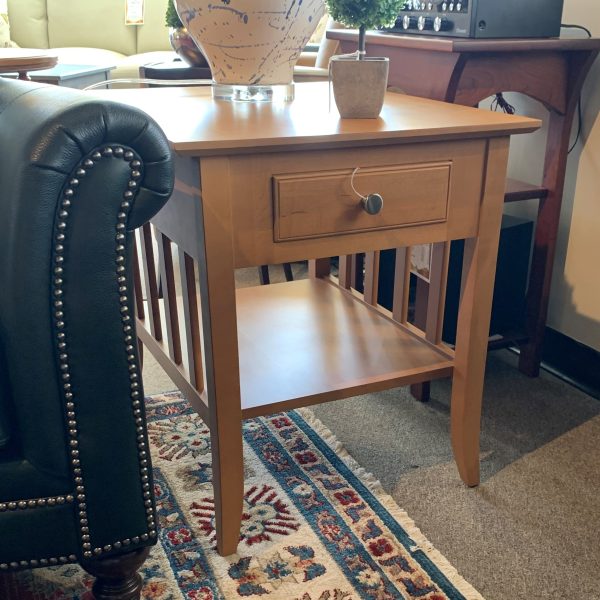 Wooden side table with small drawer and metal knob. Small plant and lamp sit on top.