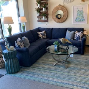 blue fabric couch with white and blue throw pillows, a glass coffee table, a blue modern side table with figurines and a frame