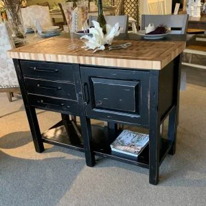 wooden island table painted black with grey chairs and a magazine on it's bottom shelf